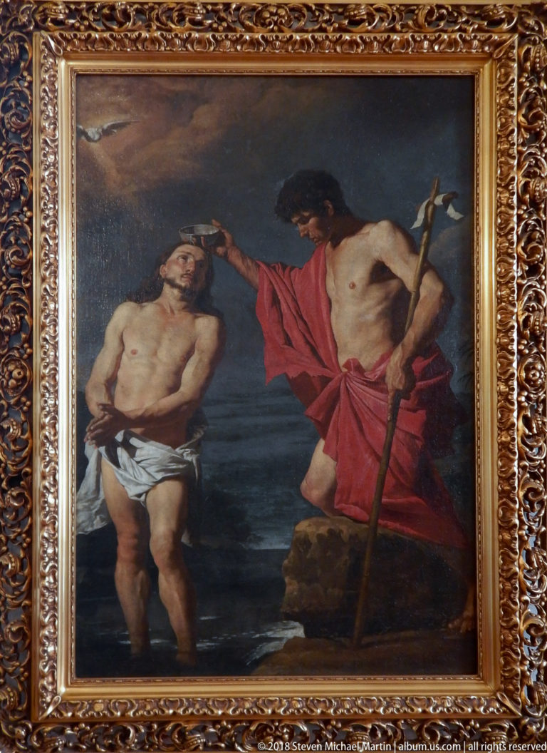 Framed painting of John the Baptist in red baptizing Christ while holding a long cross-staff.
