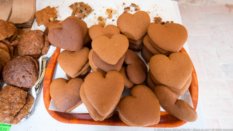 Stacked brown heart-shaped gingerbread cakes on a tray beside round and rectangular baked goods.