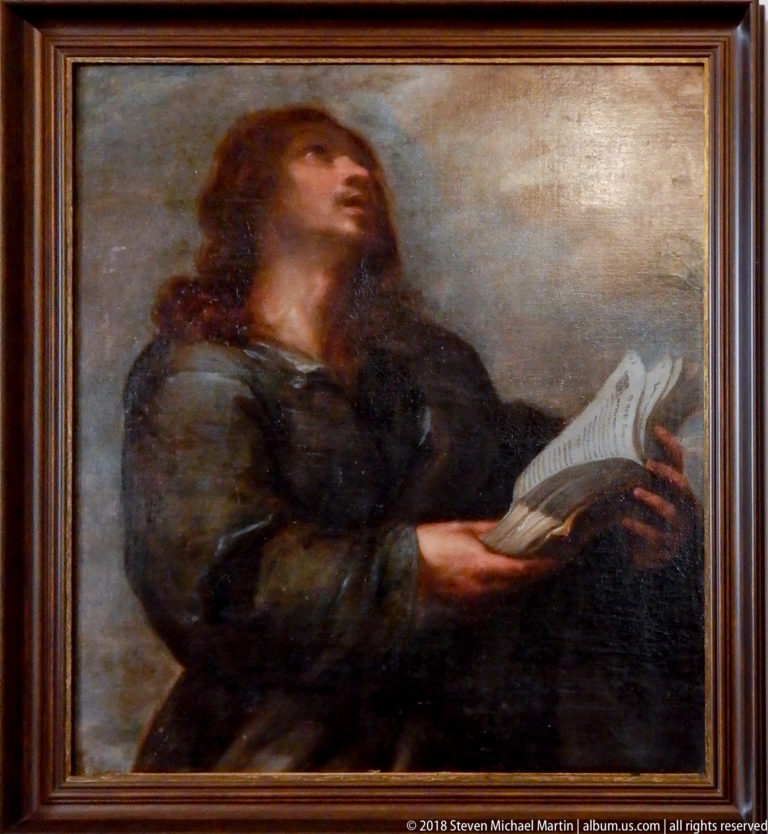 Framed painting of a long-haired man in dark robes looking upward while holding an open book.
