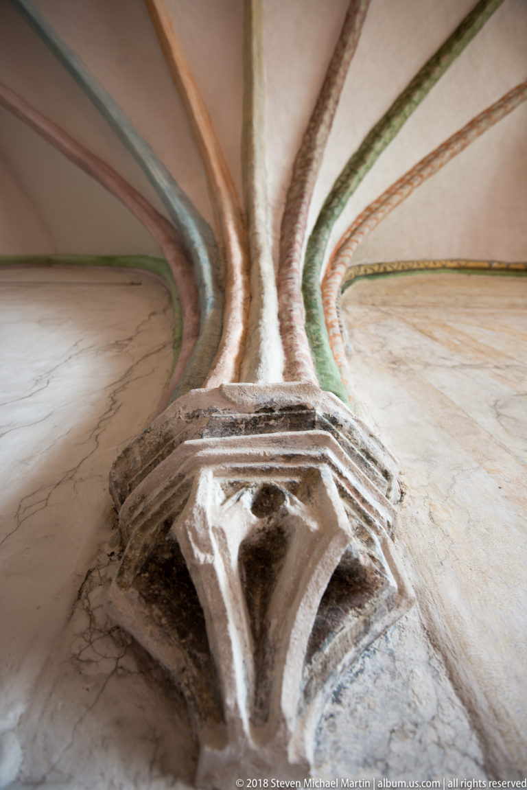 Close-up of a stone or plaster vault springing where several painted ribs rise from a worn molded support.