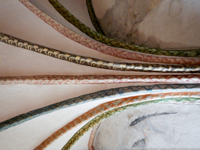 Close-up of curved Gothic vault ribs painted with multicolored repeating geometric and foliate patterns.