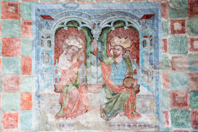 Medieval mural of two haloed enthroned figures beneath arches on a red-and-green checkerboard wall