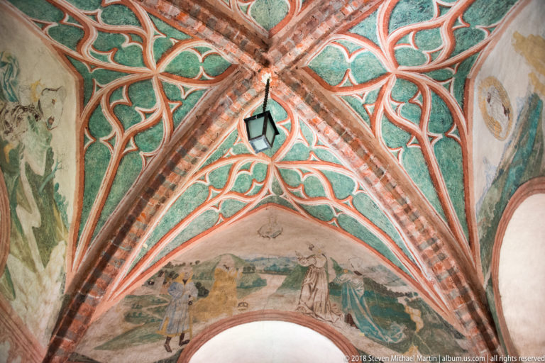 Painted Gothic vault with crossing brick ribs, green and red ornament, and faded figural murals in Lidzbark Warmiński Castle