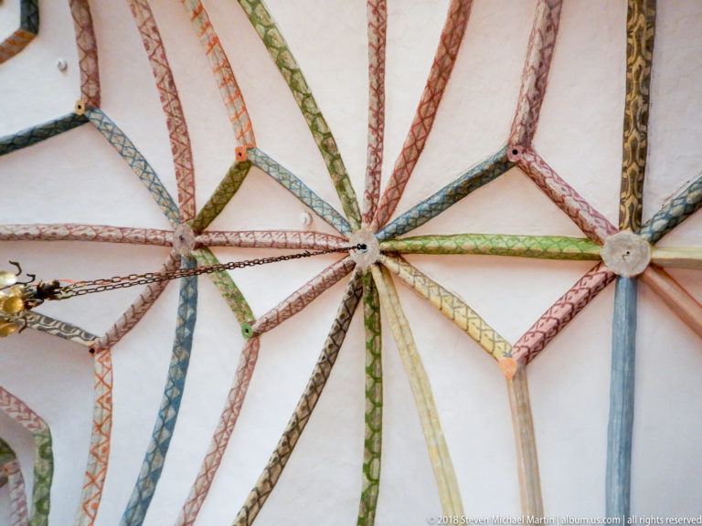 Wide upward view of a pale Gothic vault crossed by many red, green, blue, and ochre painted ribs.
