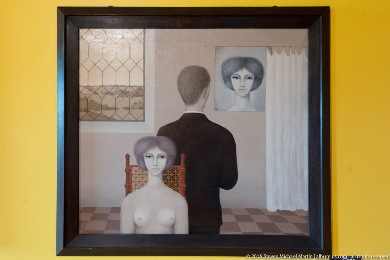 Framed contemporary painting with seated nude woman, standing man seen from behind, and a second female face behind him