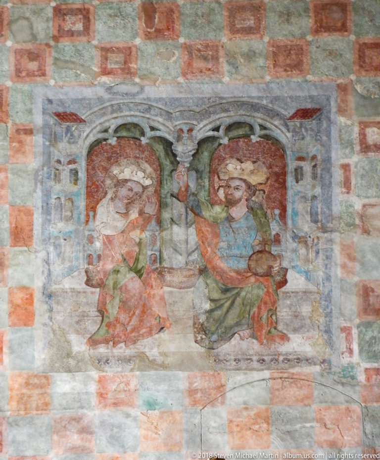 Faded wall painting of two seated haloed holy figures beneath painted arches, surrounded by a red-and-gray checker pattern.