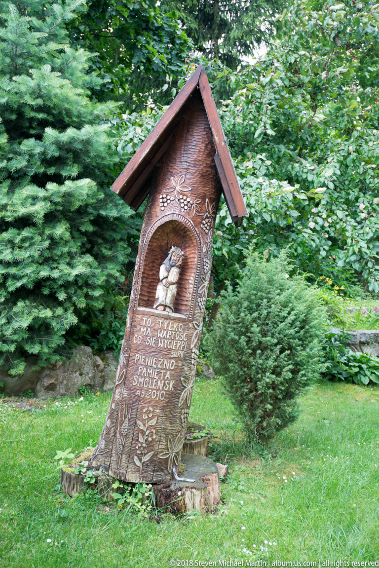 Carved wooden memorial under a small pitched roof, with a relief image, Polish inscription, and the date 2010.