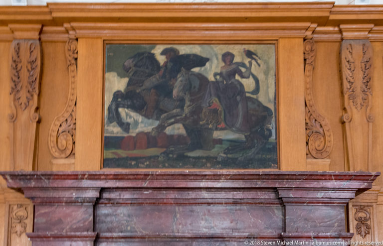 Dark figurative overmantel painting above a red marble fireplace, framed by carved wooden wall panels.