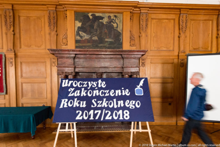 Polish sign for the ceremonial end of the 2017/2018 school year stands before a marble fireplace and wood paneling.
