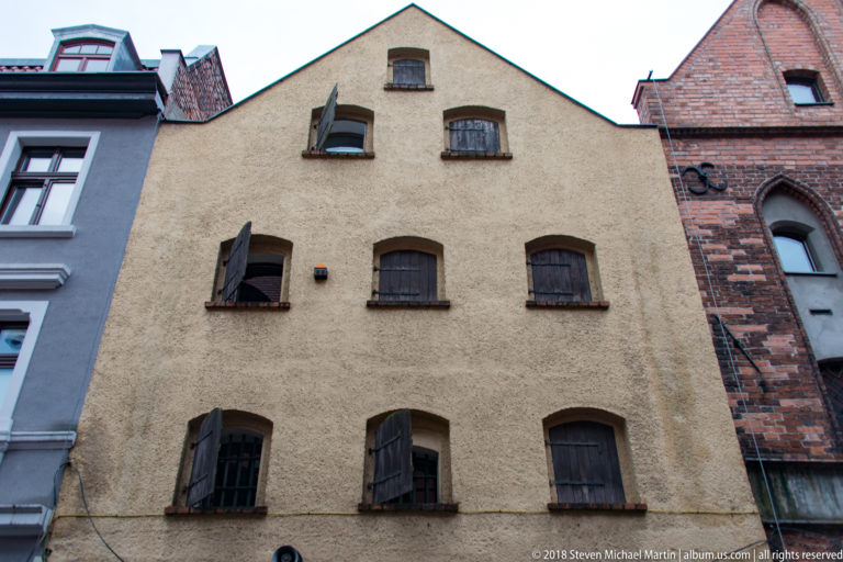 Plain historic gabled warehouse with rows of small shuttered windows in Toruń.