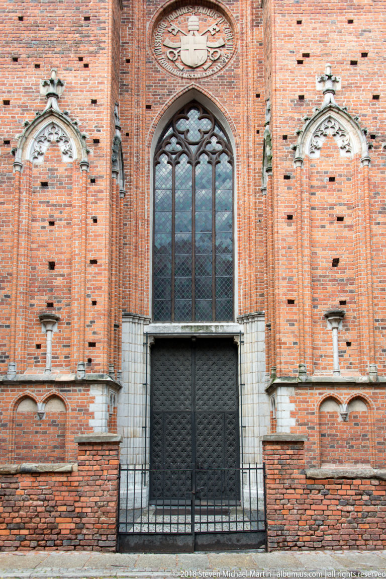 Large traceried Gothic window set in an ornate red-brick church façade in Toruń.