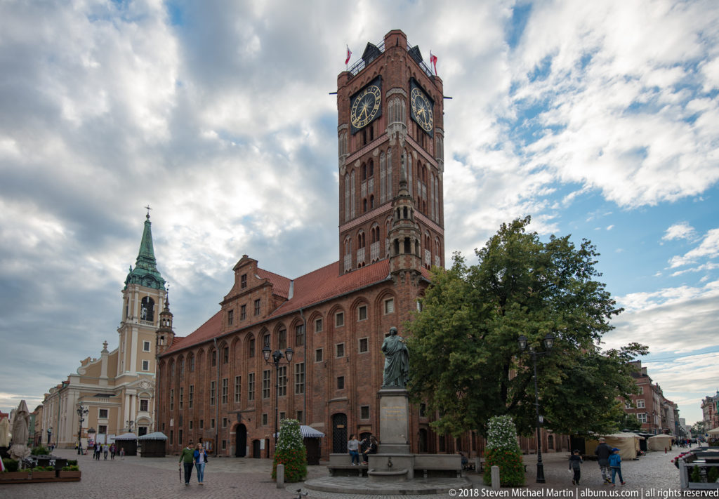 Toruń Old Town Hall and clock tower beside the Church of the Holy Spirit under dramatic clouds.