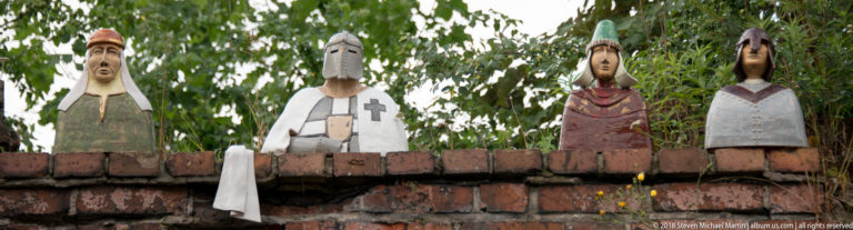 Four painted wooden figures, including a helmeted knight, standing atop a brick wall in Toruń.