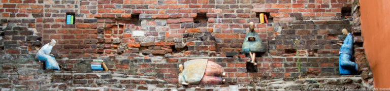 Small colorful decorative figures and objects mounted in recesses of a weathered brick wall.