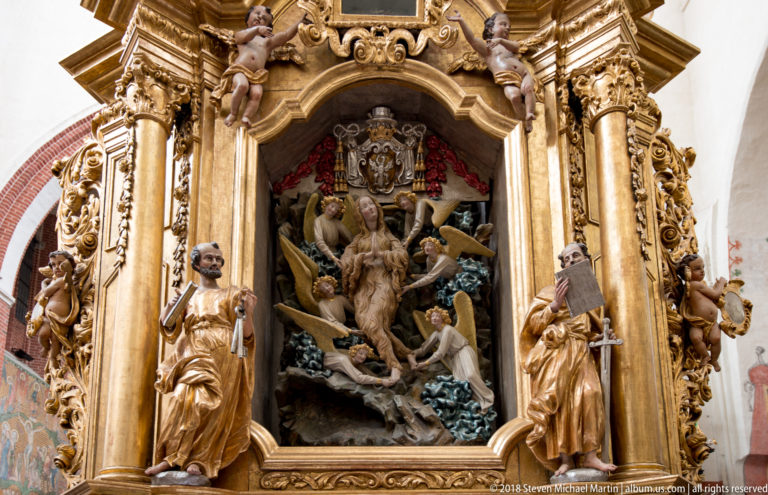 Gilded Baroque altar niche filled with carved figures, columns, scrollwork, putti, and standing saints.