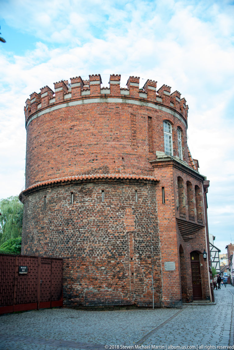 Rounded historic brick fortification building with crenellated parapet and heavy masonry walls in Toruń.
