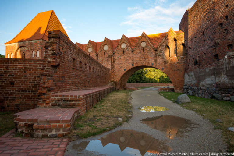 Pointed brick arch spanning a path between surviving walls of the Teutonic Castle ruins in Toruń.