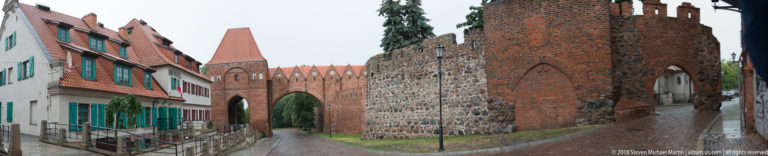 Brick-and-fieldstone medieval city wall with pointed Gothic gateway along a narrow path in Toruń.