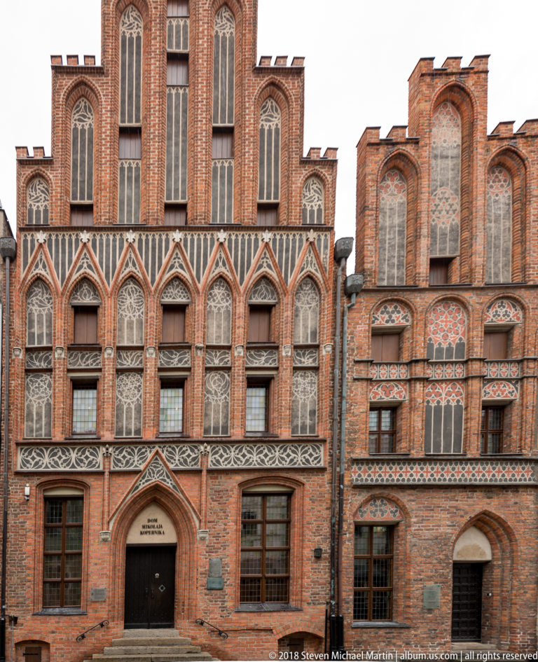 Two adjoining Gothic brick townhouse façades with stepped gables, pointed windows, decorative tracery, and the Copernicus museum entrance.