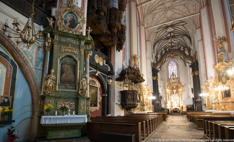 Green-and-gold Baroque side altar with saint statues beside a long Gothic nave filled with additional altars and a pulpit.