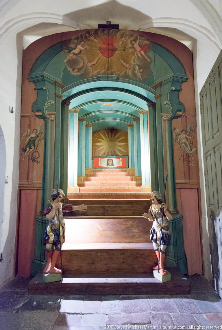 Painted perspective installation resembling a receding staircase, with small guard figures flanking the lower steps beneath a decorated canopy.