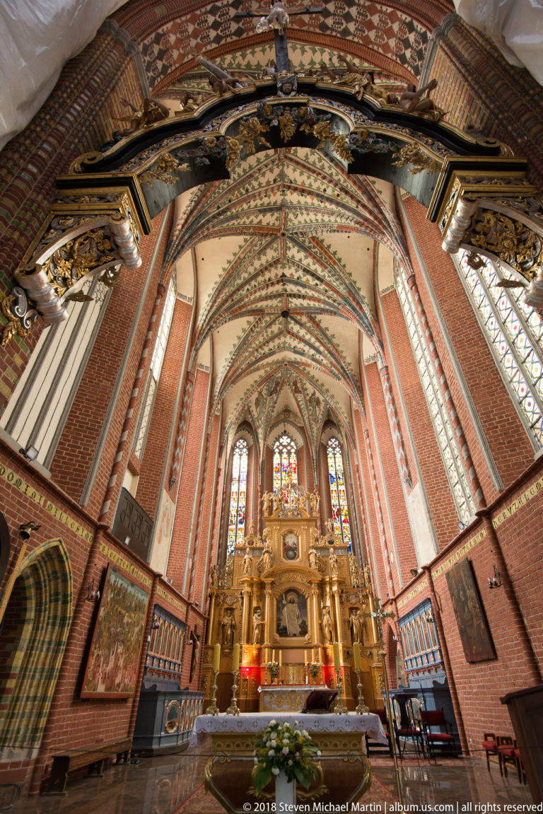 Brick Gothic church nave with rib vaults, stained glass and an ornate high altar in Toruń.