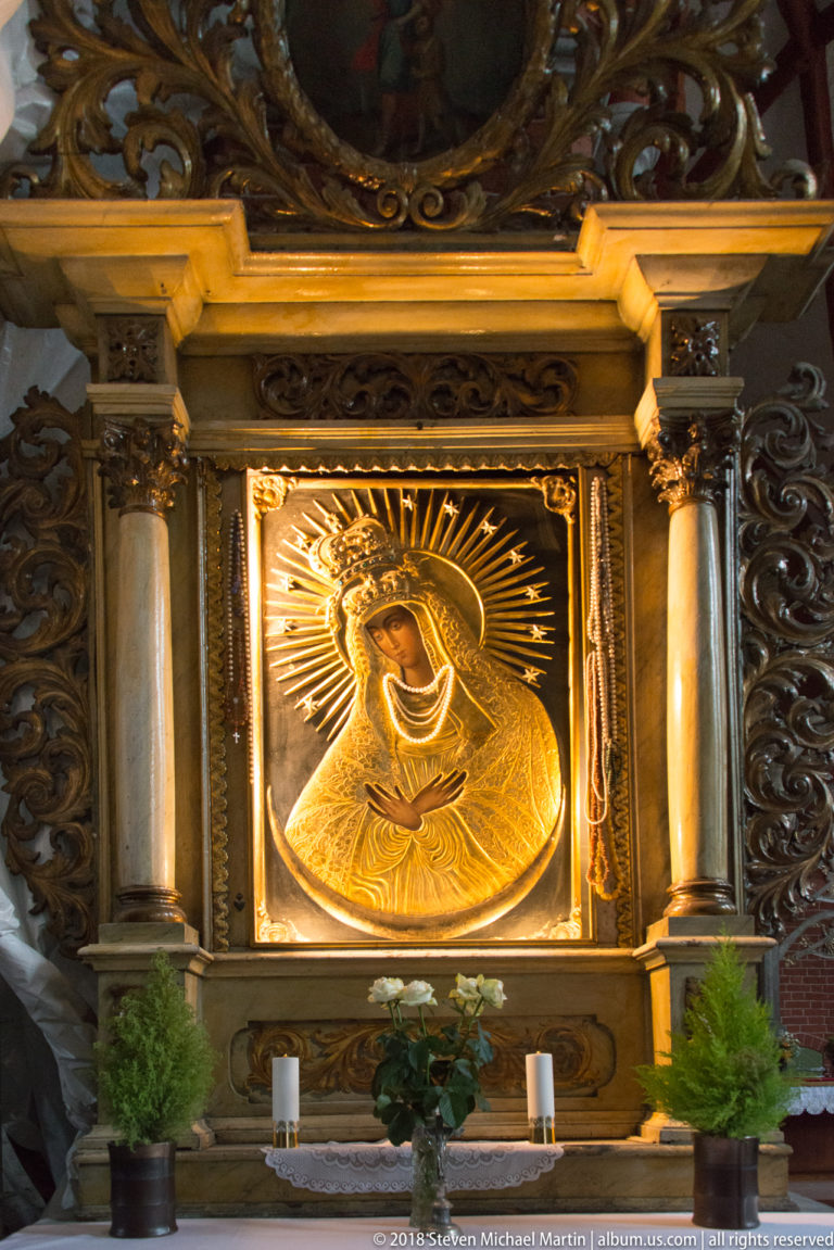 Gilded relief of the Virgin and Child framed by columns and radiating rays inside a church.