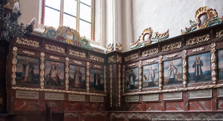Rows of painted devotional figures set into ornate carved wooden church paneling beneath a window.