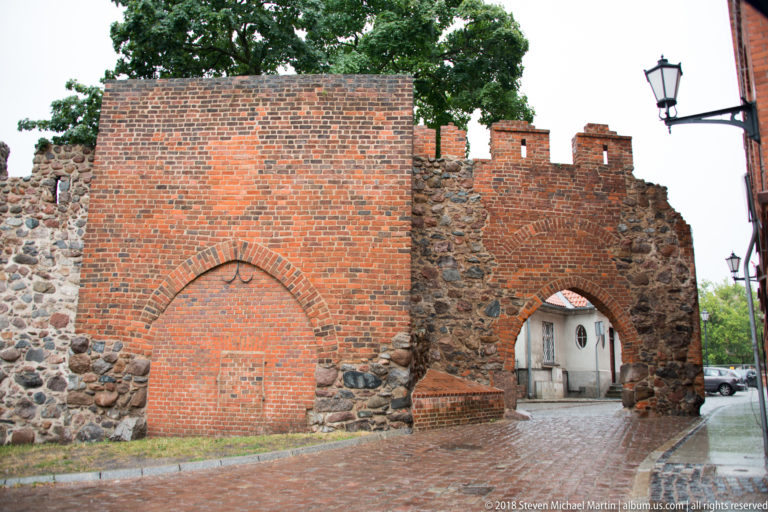 Brick and fieldstone fortification wall with a blocked pointed arch and smaller open passage.