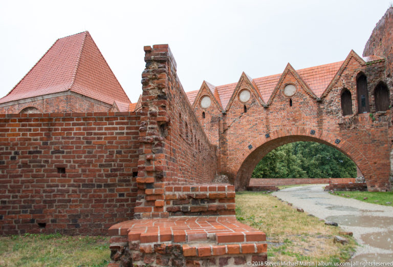 Low brick fortification wall with broad arch, triangular gables and circular openings in Toruń.