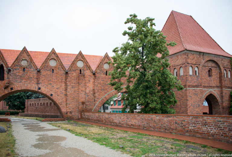 Brick medieval gateway with tiled roof and adjoining gabled fortification wall in Toruń.