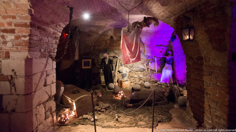 Medieval-themed museum display with figures and colored lighting inside a vaulted brick castle chamber.