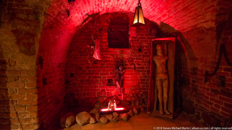 Red-lit museum installation with a human figure inside a brick-vaulted chamber of the castle ruins.