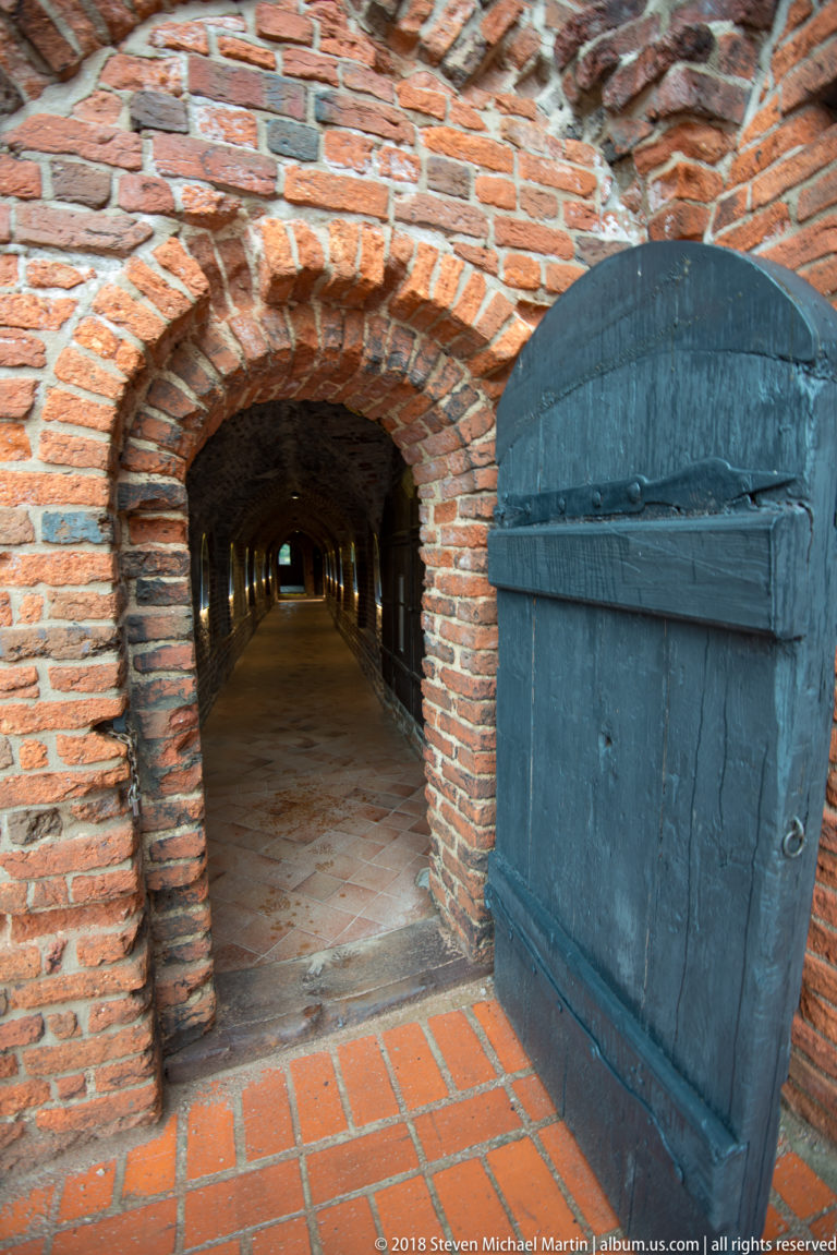 Open heavy wooden door leading into a long low brick-vaulted passage in the castle ruins.