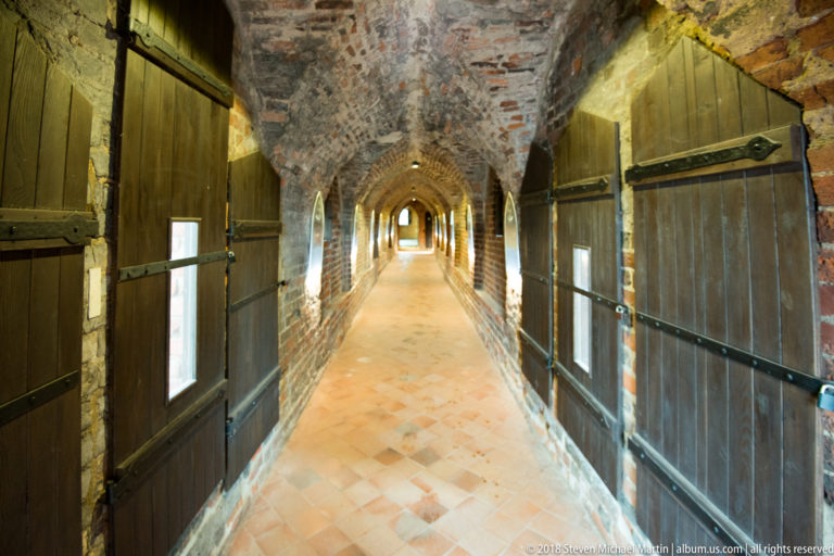 Long brick-vaulted castle corridor lined with heavy wooden shutters and a tiled floor.
