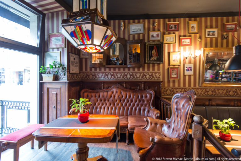 Cozy historic-style café or pub interior with leather seating, wood furniture, lamps and framed pictures.