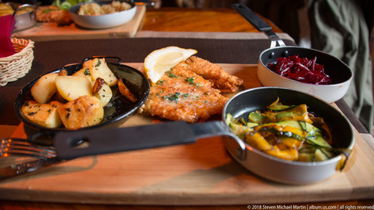 Restaurant meal with breaded cutlet, roasted potatoes, cucumber salad and shredded beetroot.