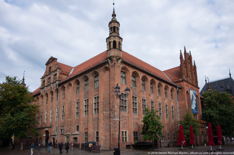 Red-brick Old Town Hall in Toruń with tall central tower, tiled roof and Gothic windows.