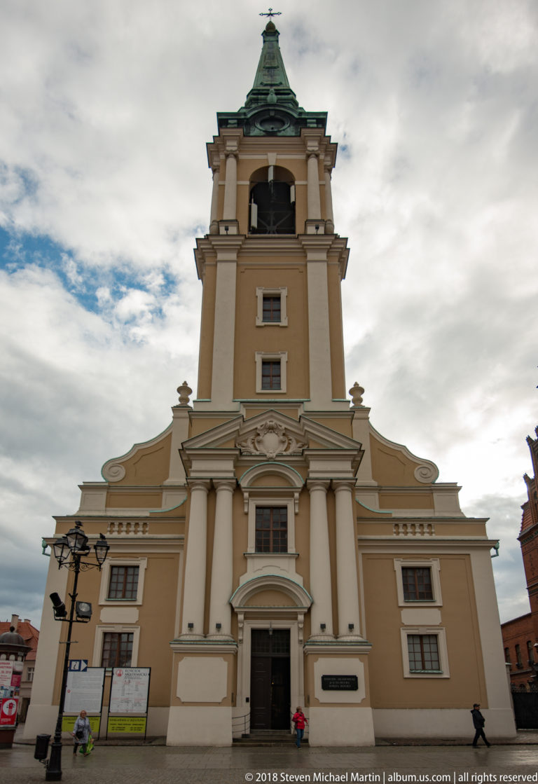 Church of the Holy Spirit in Toruń with pale façade, square tower and green copper roof.