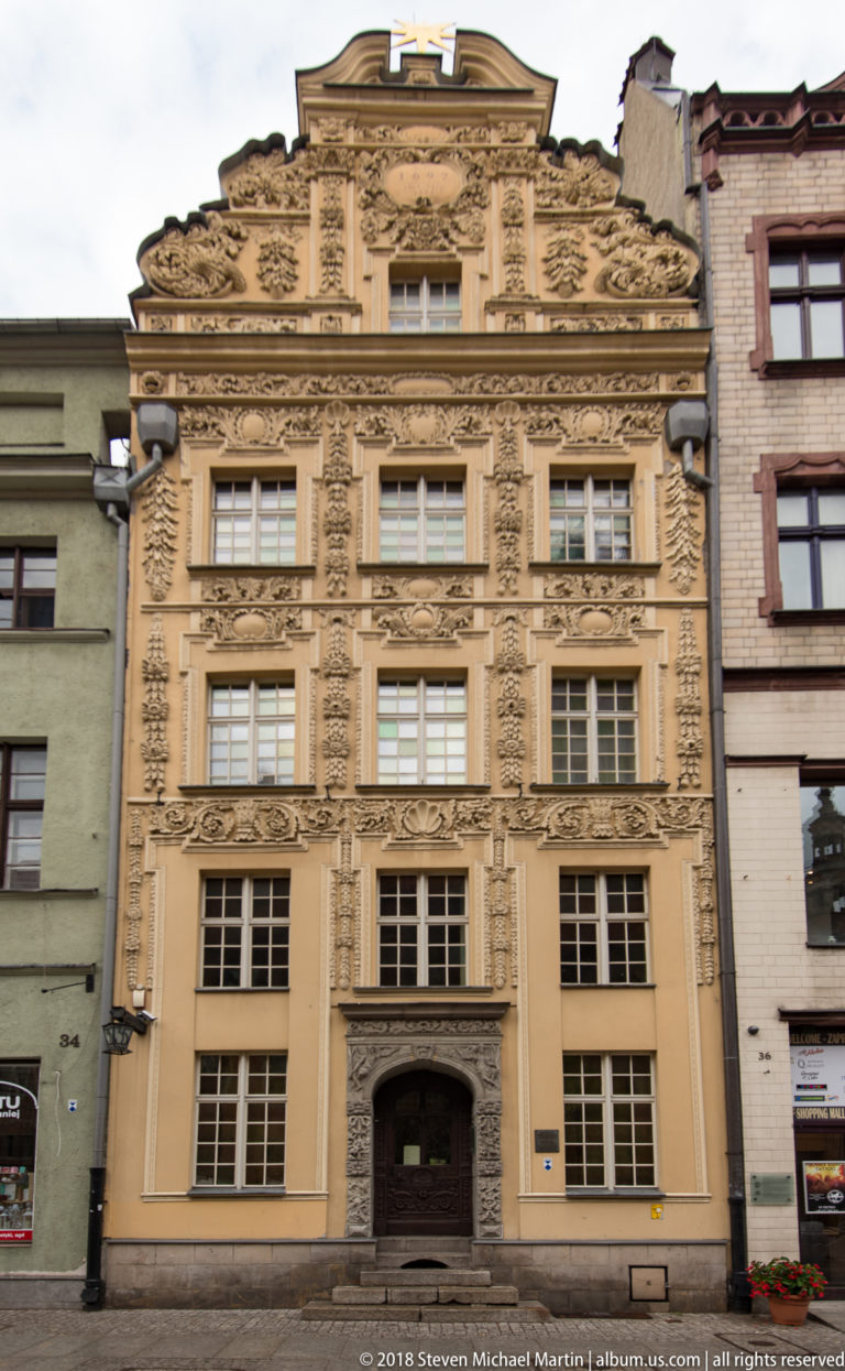 Ornate pale stucco townhouse façade with dense floral and scrollwork decoration in Toruń.