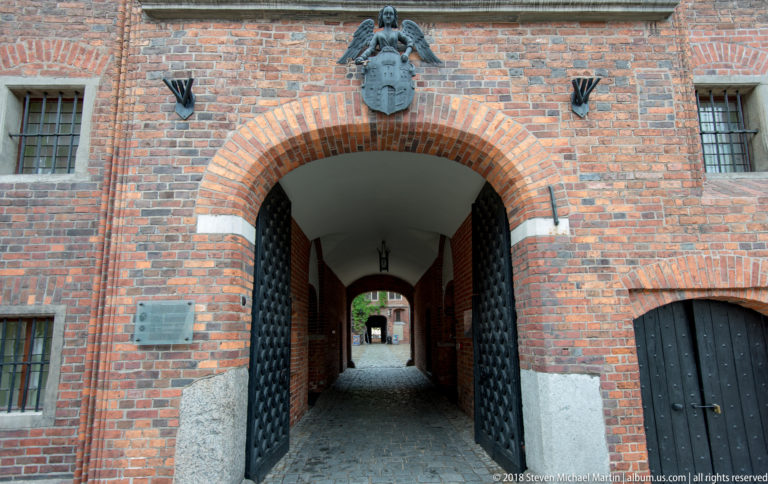 Brick arched passage with heavy studded doors and coat of arms above the entrance.