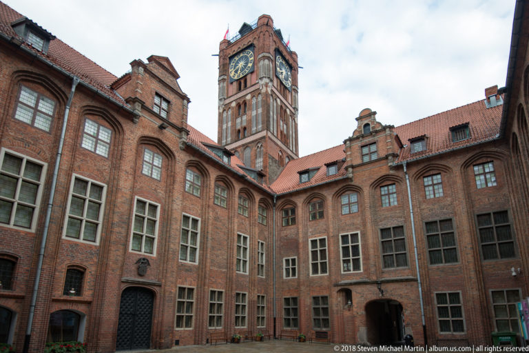 Brick courtyard of Toruń Old Town Hall with tall clock tower rising above surrounding wings.