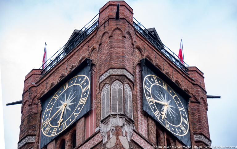 Close view of two large clock faces on adjacent sides of Toruń Old Town Hall tower.