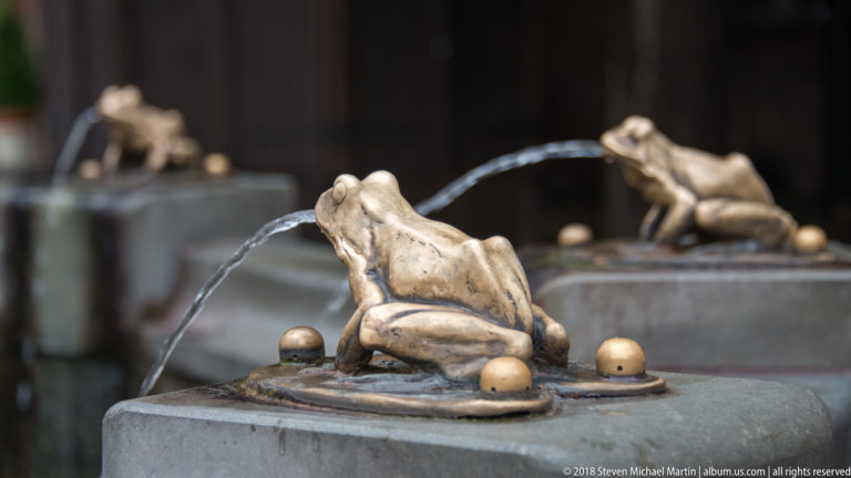 Bronze frog fountain figures spouting water near Toruń Old Town Hall.