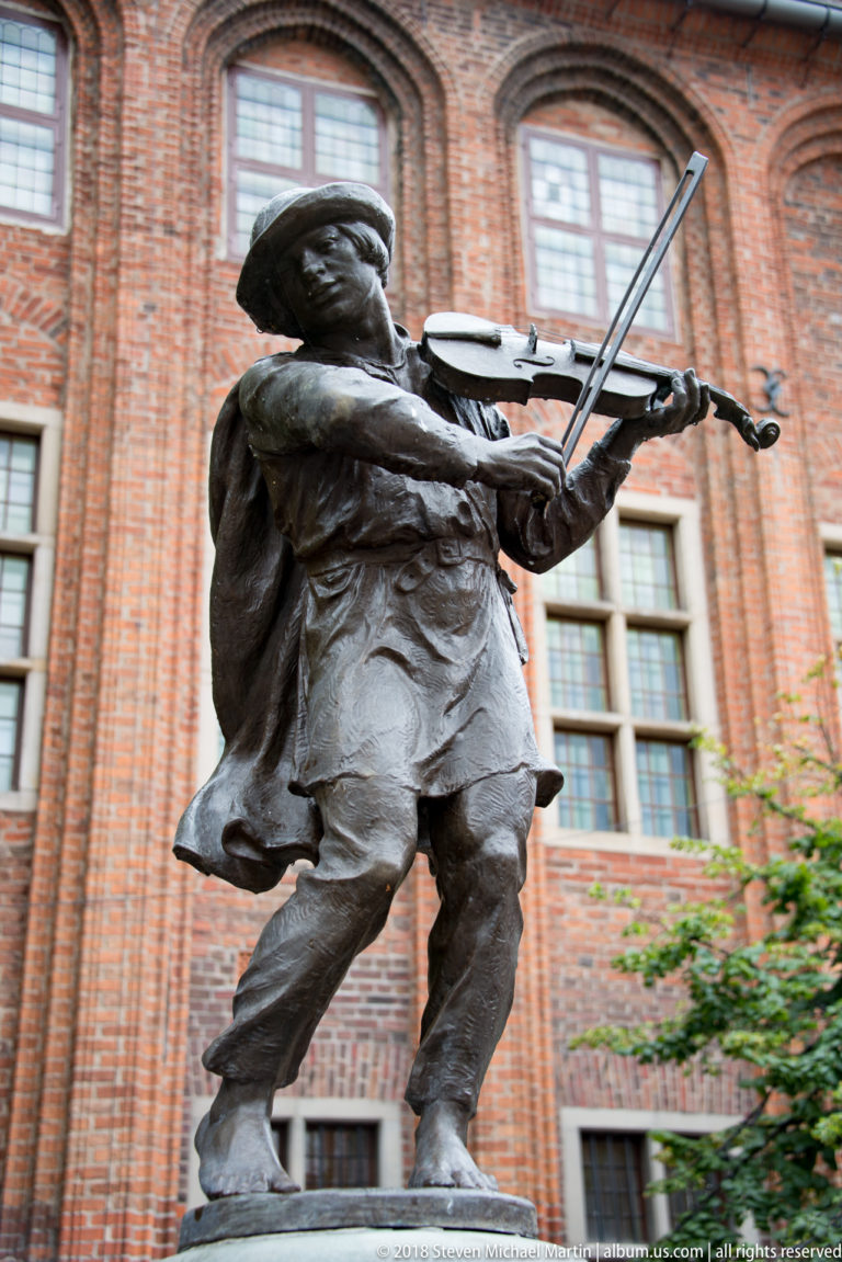 Bronze fiddler of the Flisak fountain playing violin in front of Toruń Old Town Hall.