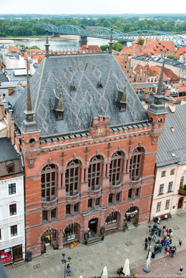 Elevated view of ornate red-brick civic building with steep roof and arched windows on Toruń market square.