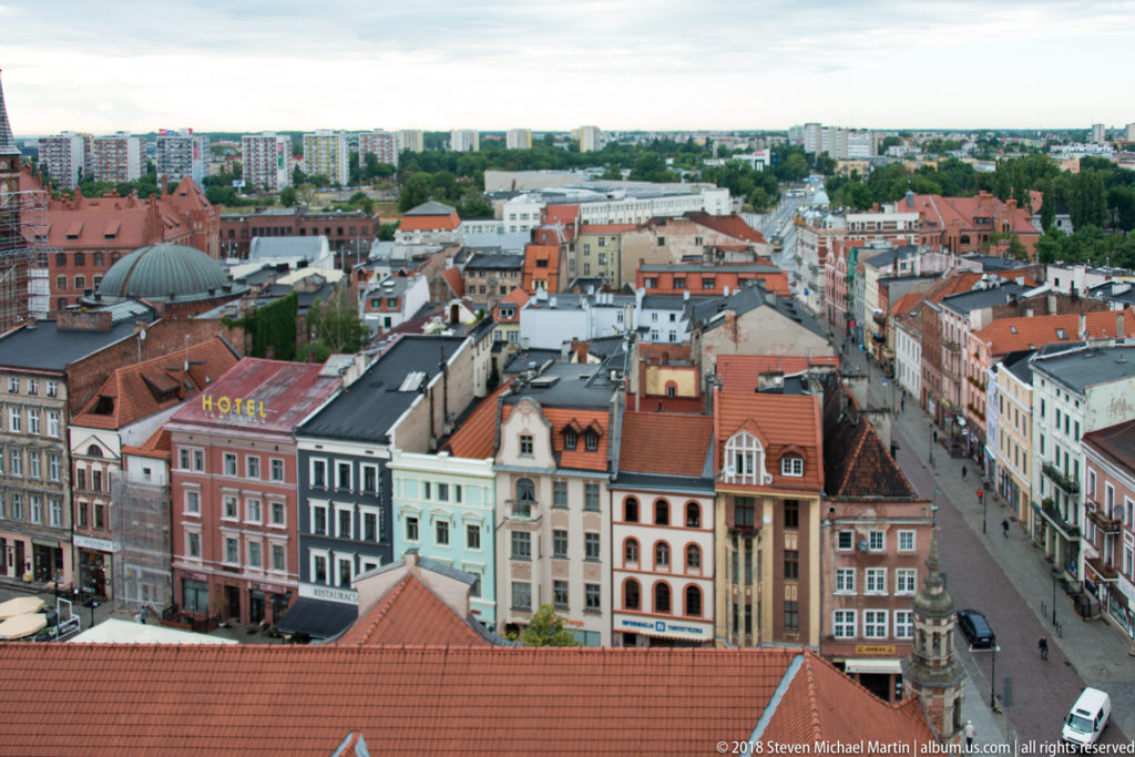 Elevated view over colorful historic façades, red-tiled roofs and a main street in Toruń Old Town.