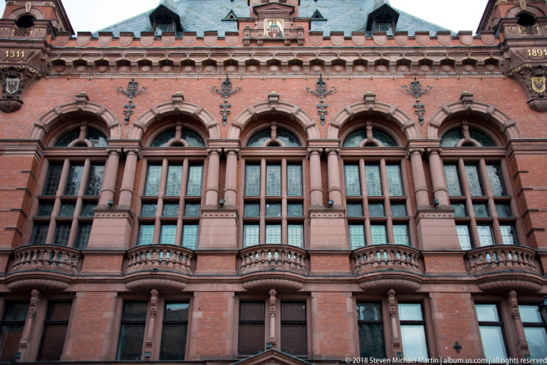 Close view of ornate red-brick façade with tall arched windows, columns and small stone balconies.