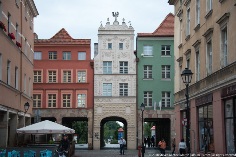 Ornate white gabled townhouse with relief decoration and an arched passage between colorful buildings in Toruń.