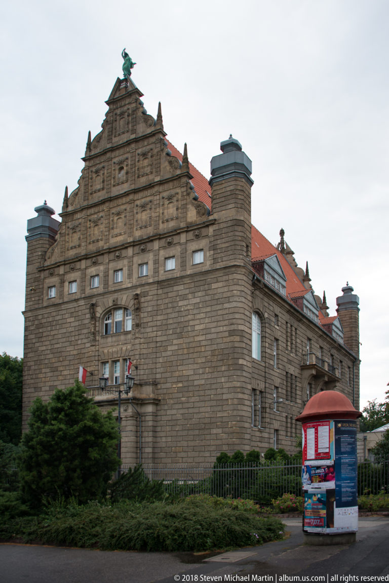 Large historic masonry building with stepped central gable, small windows and corner towers in Toruń.